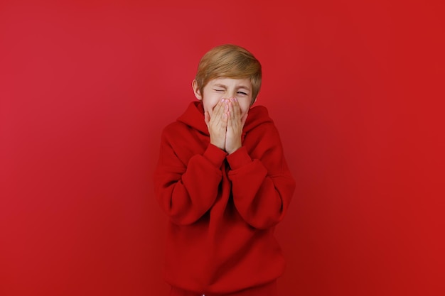 A frightened boy in a red tracksuit clutched his face with his hands