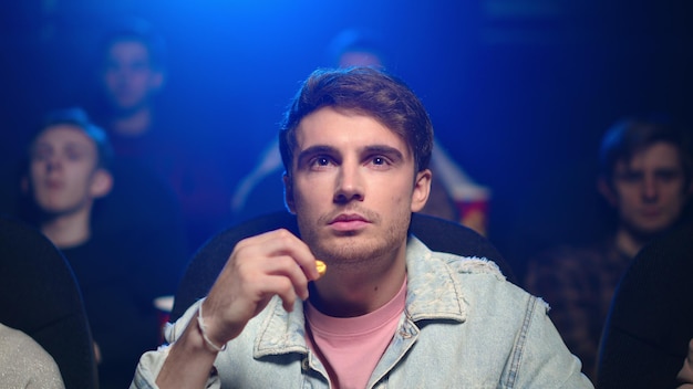 Frightened man watching horror film with wide open eyes in movie theater