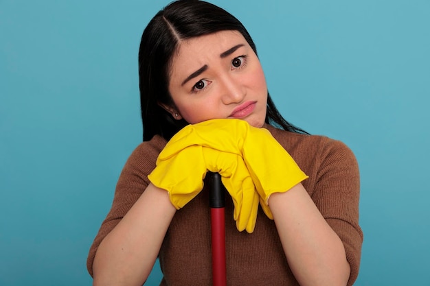 Frightened sad asian housewife holding on brush stick yellow gloves holding on brush stick, Cleaning home concept ,Housekeeper feeling negative exhausted taking some rest