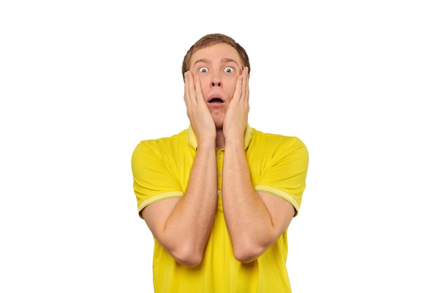 Frightened young man in yellow Tshirt holding hands over face white background afraid negative