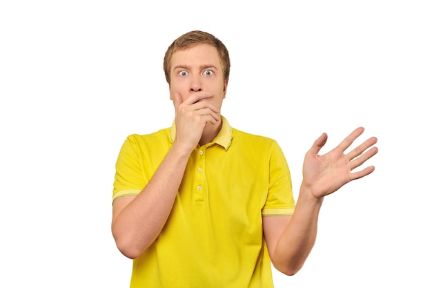 Frightened young man in yellow Tshirt holding hands over face white background afraid negative