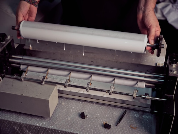 From above of crop anonymous male bookbinder putting roller with glue into machine while working at workbench in professional workshop