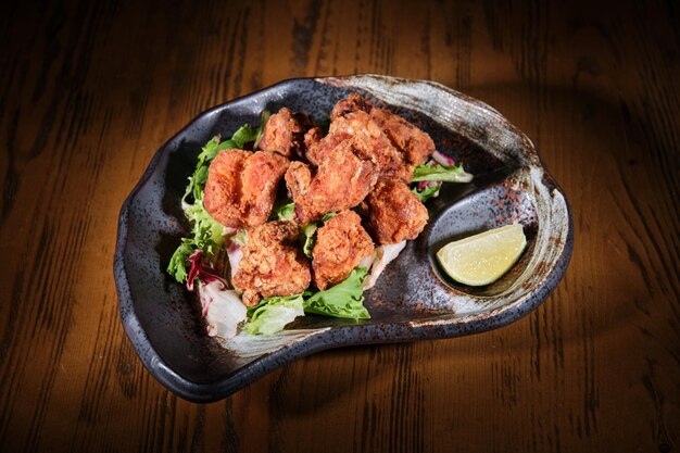 From above of crunchy deep fried chicken wings on pile of salad leaves served on plate with wedge of lime