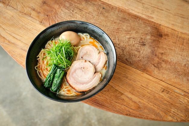 From above of delicious Japanese ramen with noodles rolled pork nori and broth served in bowl and placed on round wooden table in restaurant