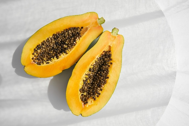 From above of fresh organic ripe yellow papaya fruit halves with seeds placed on gray table in sunlight in studio