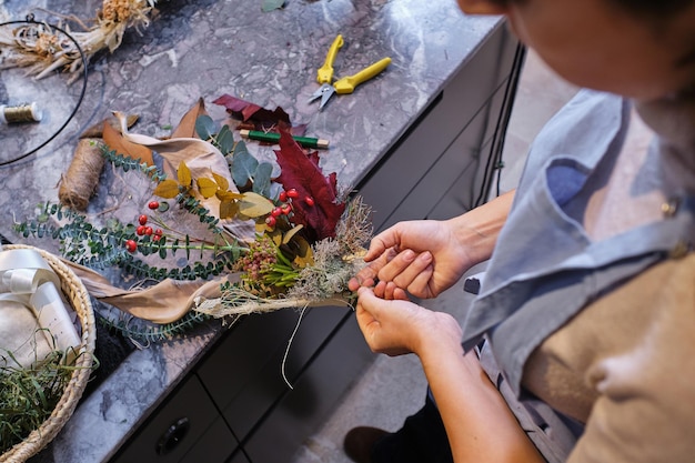 From above side view of unrecognizable female florist tying bunch of flowers on table while making bouquet at work