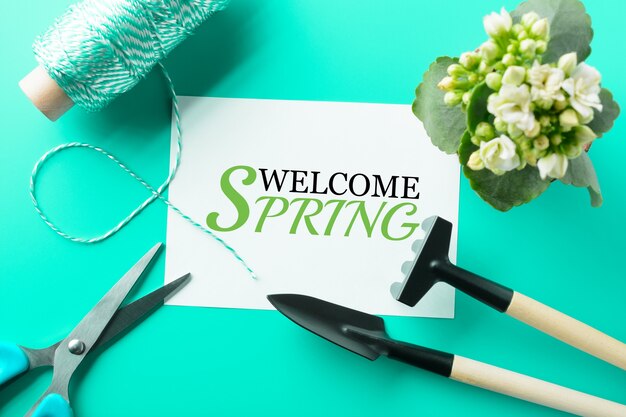 From above Welcome Spring words and different instruments for gardening on the turquoise table