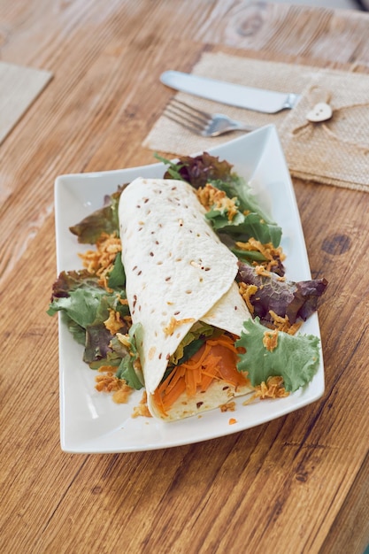 From above of yummy vegetable shawarma with carrot cucumber and lettuce served on white ceramic plate on wooden table