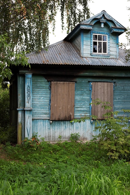 Front exterior old historic abandoned wooden painted blue house with boarded up windows