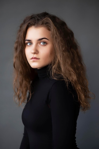 Front image portrait of a girl with curly hair dressed in a black on a grey background