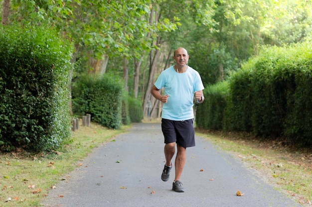 Front portrait in landscape format of a senior man running along a path among the green trees of a park