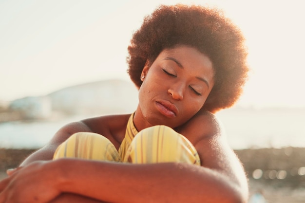 Front portrait of pretty young black girl relaxing with closed eyes in outdoor with sunlight in background Concept of meditation serene people Loving yourself lifestyle people Afro hair style model