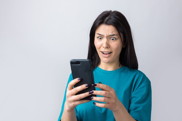 Front portrait of young smiling woman using mobile phone against grey background