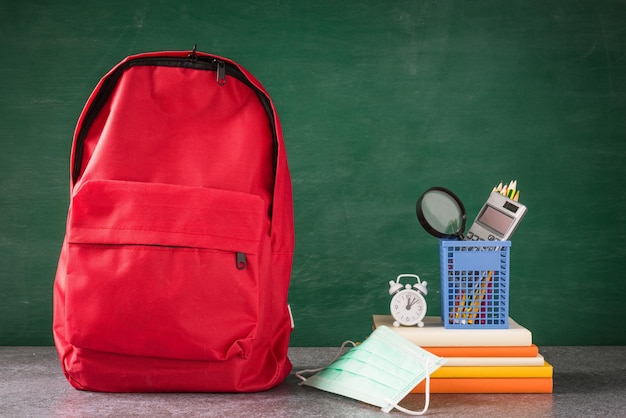 Front school backpack and accessories with face mask protect on desk at green chalkboard, student bag at classroom backboard, Back to school education new normal outbreak COVID-19 or coronavirus