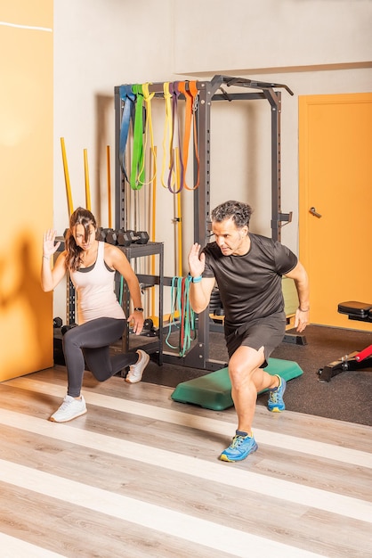 Front side view of athlete woman and man doing lunges exercises for leg muscle workout training in gym. Concept of exercises in gym.