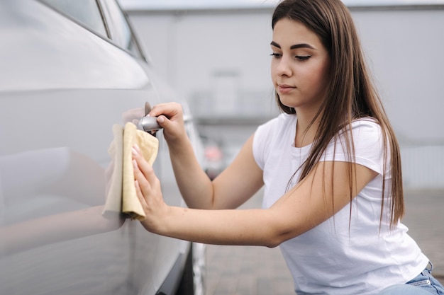 Front view of attractive happy joyful female driver washing her car with special rag in selfservice