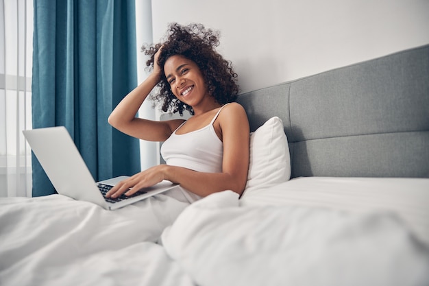 Front view of an attractive smiling female freelancer touching her curly hair with one hand