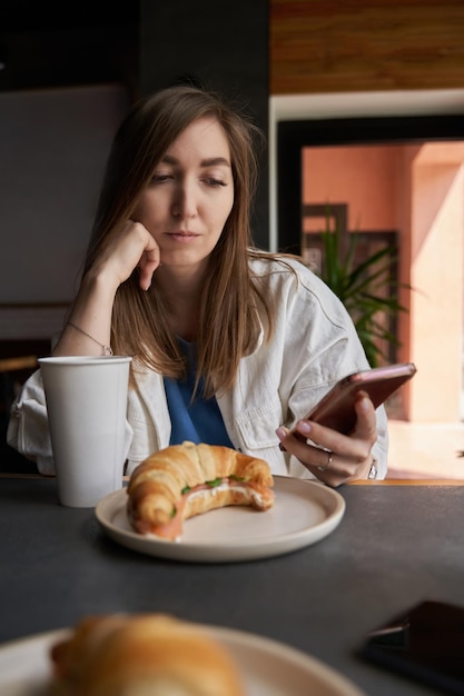 Front view of attractive woman wearing glasses using smartphone drinking coffee in cafe Female texting and sharing messages on social media enjoying mobile technology relaxing in coffee shop