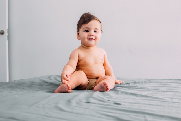 Front view of beautiful smiling baby sitting on the bed in the room