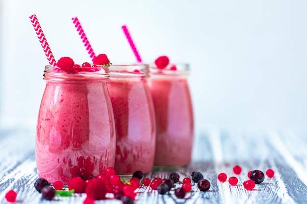 Front view of berries milkshakes in glasses jars with ingredients on wooden table Space for text