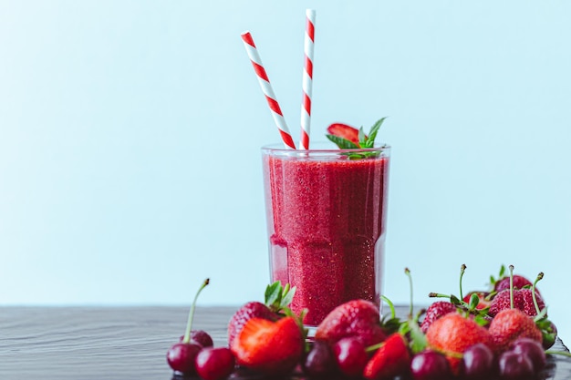 Front view of berry juice or smoothie with fresh strawberries and cherries on blue background