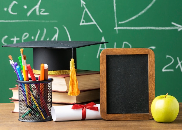 Front view of blackboard with academic cap and pencils