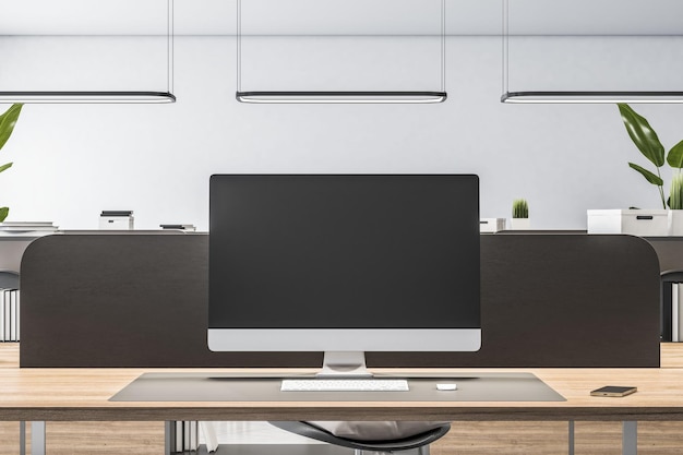 Front view on blank black monitor screen with place for your logo or text on wooden workspace table in minimalistic style office with black partition on light wall background 3D rendering mock up