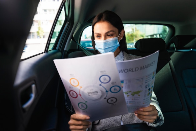 Front view of businesswoman with medical mask in the car reviewing documents