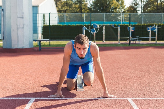 Front view of a Caucasian male sprinter in a race starting position hands on the line and legs