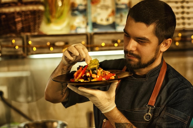 Front view of chef holding dish with delicious vegetable salad and looking at it chef checking ingredients of salad concept of culinary food and gastronomy