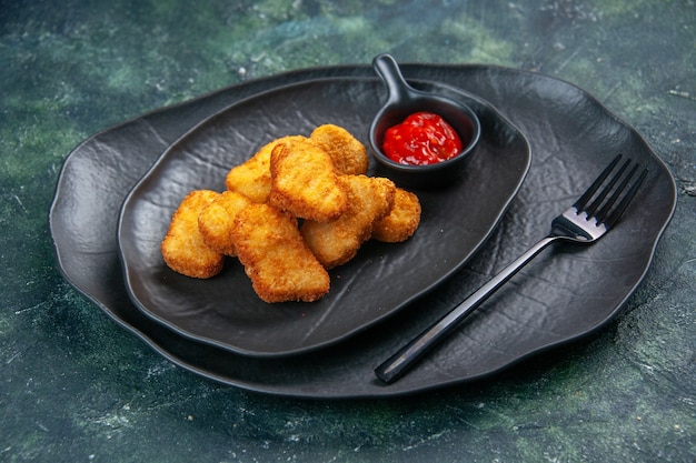 Front view of chicken nuggets and ketchup fork in black plates on dark surface