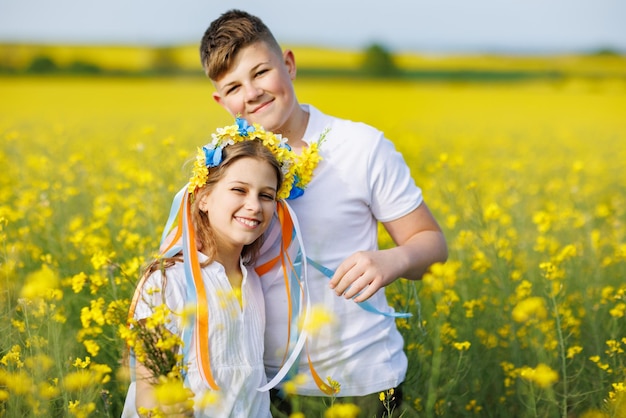 Front view of children brother and sister walking far away along path with grass surrounded by yellow fields