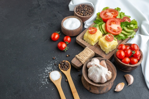 Front view of chopped and whole fresh vegetables on cutting board in bowls and spices on white towel on black surface