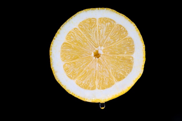 Front view close up photo of half a lemon on a black background with a drop of juice falling