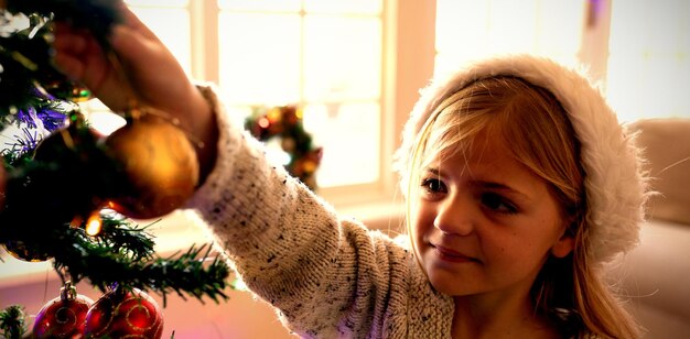 Photo front view close up of a young caucasian girl decorating the christmas tree in her sitting room at christmas time