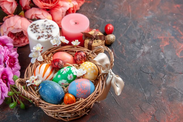 front view colored easter eggs inside basket with flowers and biscuits on dark surface