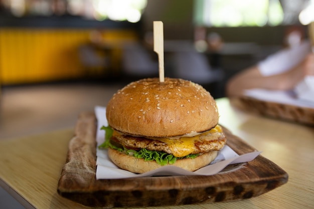 Front view of crispy burger on wooden plate at the fast food cafe