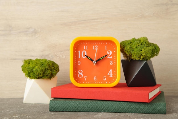 Front view desk with clock books and plant on light background Copy space