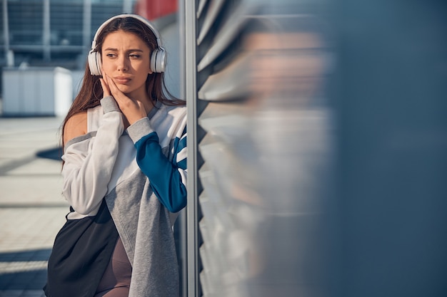 Front view of a despondent Caucasian athlete in headphones touching her cheek with both hands