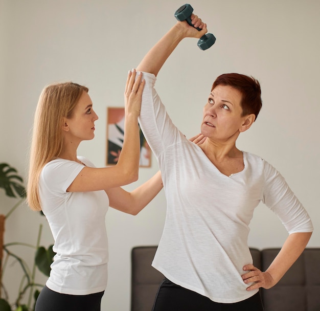 Front view of elder woman in covid recovery doing exercises with nurse and dumbbells