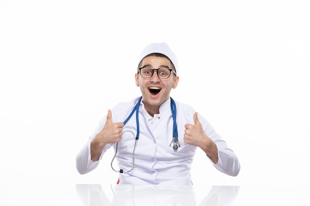 Front view excited male doctor in medical suit sitting behind desk