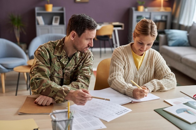 Front view father wearing military uniform helping daughter with homework