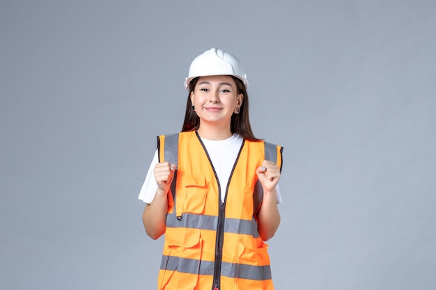 Front view of female builder in uniform smiling on white wall