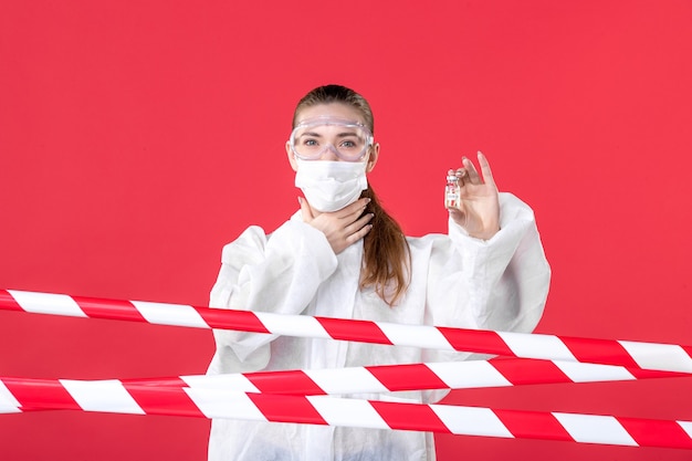 front view female doctor in protective suit and mask holding little flask on red background crime virus line covid- hospital cure nurse