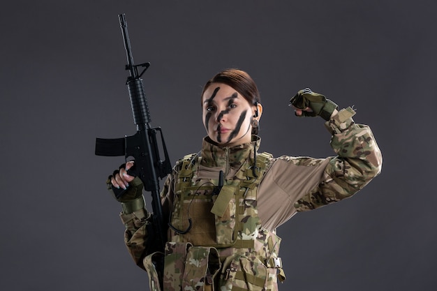 Front view female soldier in camouflage with machine gun on the dark wall