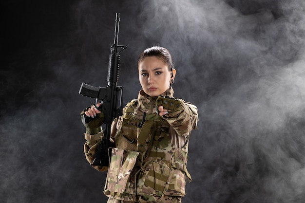 Front view of female soldier in uniform with rifle on black wall