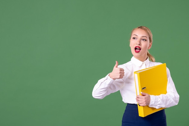 Front view female teacher holding yellow files on green background school lesson book work student uniform library study