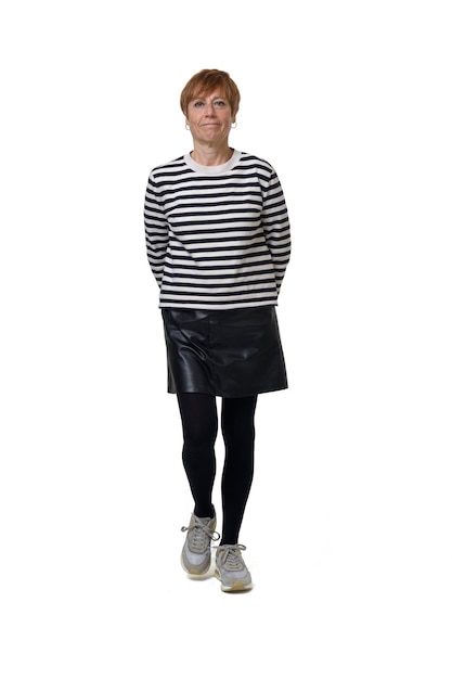 Front view full length portrait of a woman in skirt striped sweater and sneakers walking and looking at camera on white background