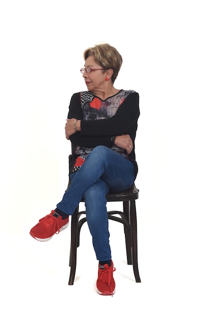 Front view of a full portrait of happy senior woman sitting on chair looking away on white background