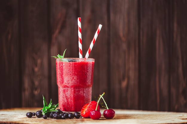 Front view of glass with fresh crimson smoothie with summer berries on wooden background Good food